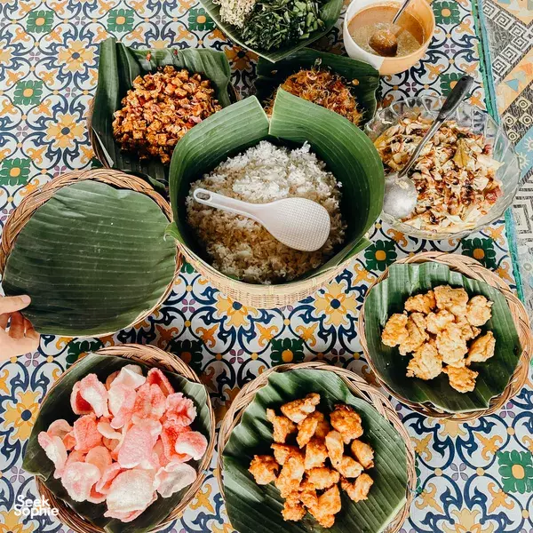 Assorted Lombok-style dishes arranged on woven baskets and banana leaves, including rice, grilled chicken, and prawn crackers
