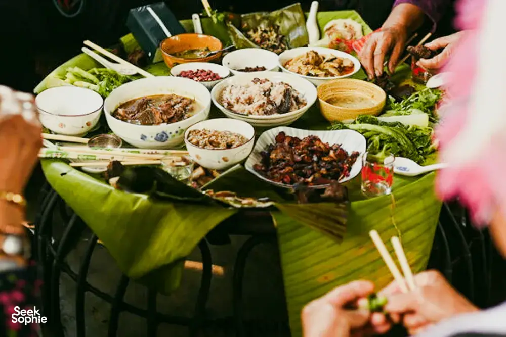 Santap bersama di Xishuangbanna dengan banyak hidangan tersaji di atas daun pisang, tangan-tangan menyiapkan dan menyajikan herba kepada para tamu