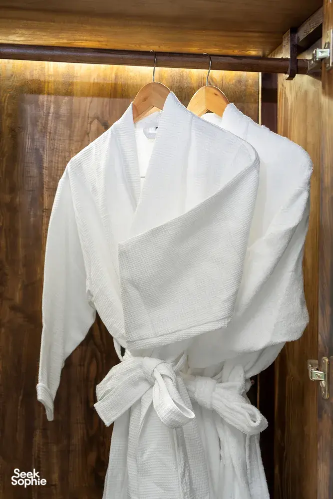 White bathrobe hanging on coat hooks inside a wooden wardrobe in Cat Ba Ocean Cruises’ cabin on the 3D2N Cat Ba cruise