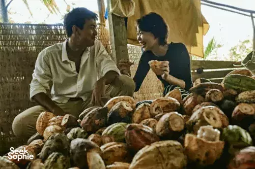 Two guests chatting at a stall of cocoa pods and fruit during a cycling add-on with The Island Lodge in the Mekong Delta