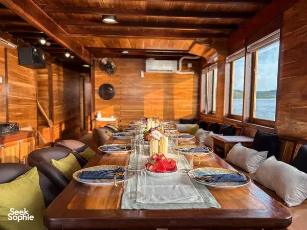 Dining table set with plates, cutlery and drinks in the wooden onboard lounge of the Archipelago Reserve Komodo liveaboard, Labuan Bajo