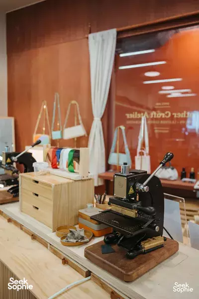 Crafune leathercraft studio in Singapore: sewing and cutting machines on wooden benches with hanging tote bags — workshops in Singapore
