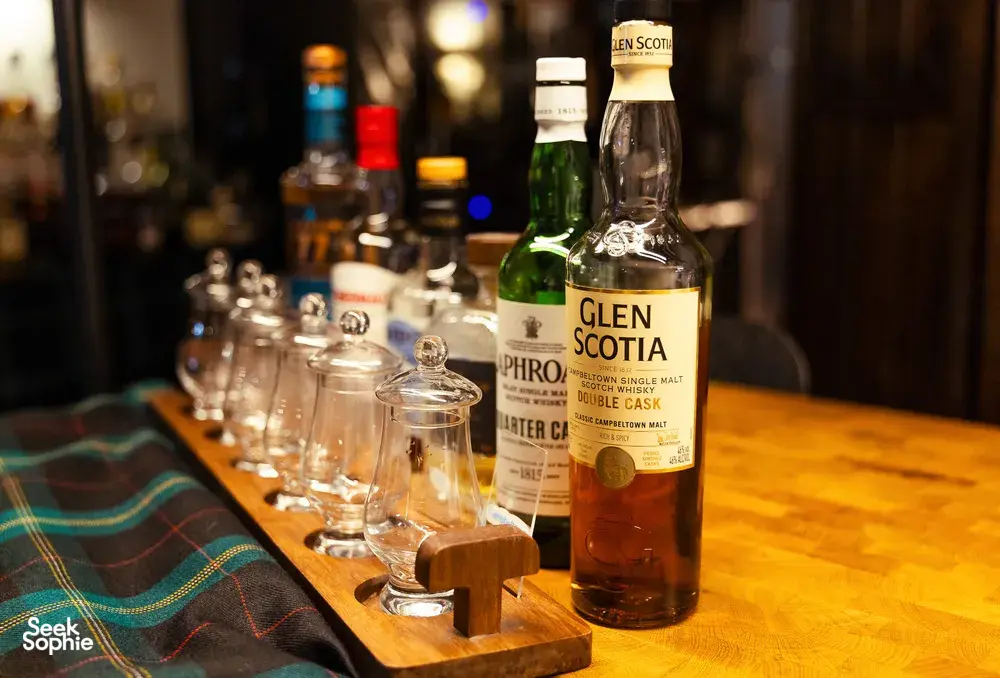 Glen Scotia whisky bottle and neat tumbler glasses on a wooden bar in a hidden home bar for Scotch & Sambal private dining Singapore
