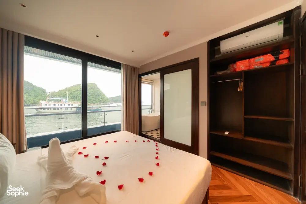 King bed in Cat Ba cruise cabin with floor‑to‑ceiling windows overlooking the bay and limestone hills