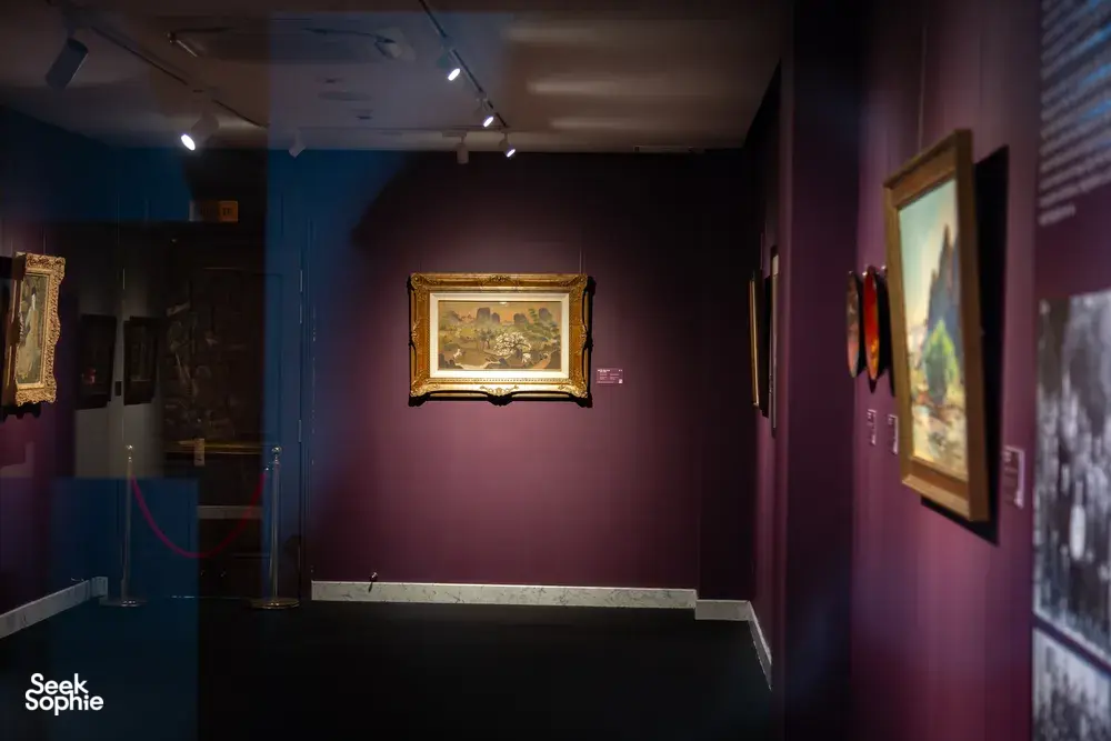 Gallery corridor with framed Vietnamese artworks on purple walls, track lights and rope barrier at Quang San Art Museum in Ho Chi Minh City