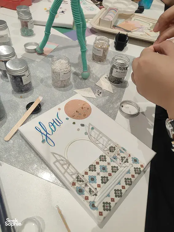 Hands arranging a gemstone vision board at Gemstory in Singapore, surrounded by jars, brushes, and paper crafting materials