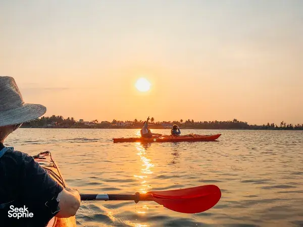 Close view of a kayak paddle as another boat of paddlers heads towards sunset on a Hoi An Kayak Tour in Hoi An