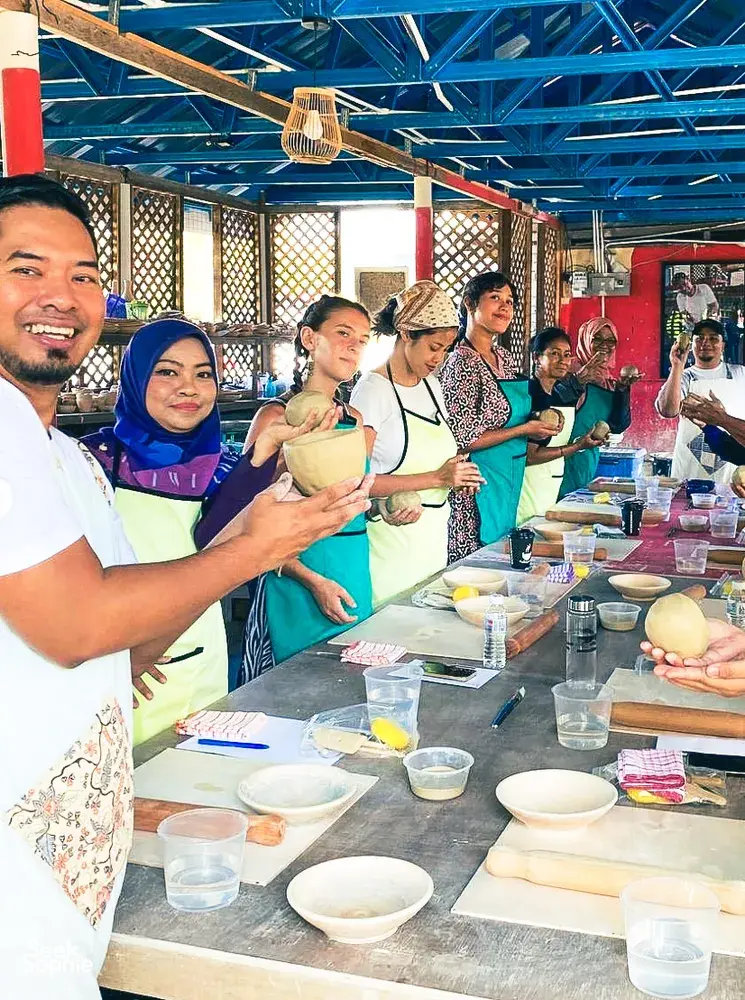 Group pottery class at Ilham Ceramic Studio in Langkawi with participants glazing clay bowls on a shared worktable