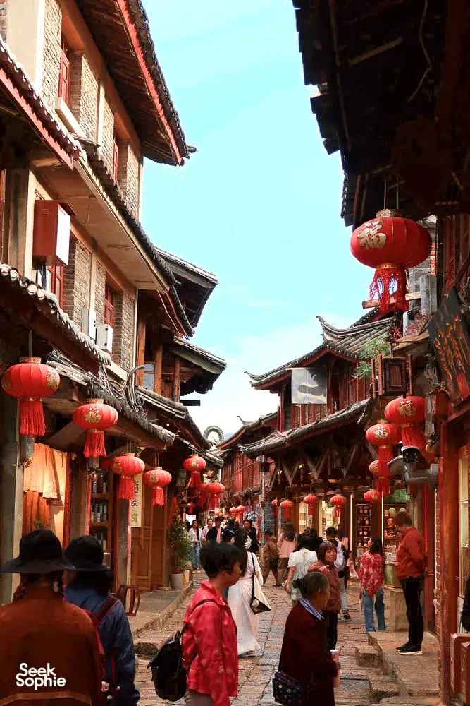 Lantern-lit walkway through Lijiang’s Shuhe Ancient Town, with Naxi-style buildings and people strolling along the lane