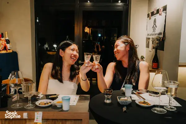 Guests toast at a rare sake tasting dinner in Singapore, smiling across a table of small dishes and shared glasses