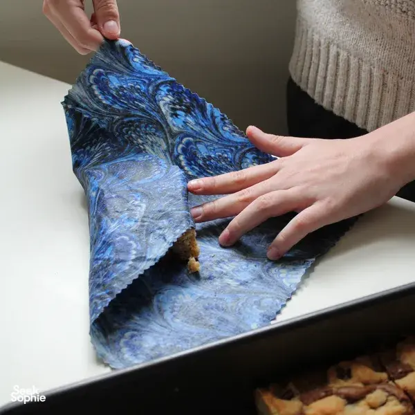 Hands pressing a blue patterned cotton sheet onto a tray to form reusable food wraps in Singapore during workshops in Singapore