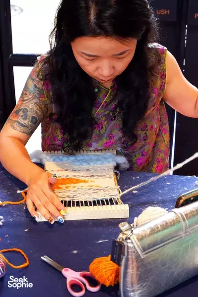 Woman weaving at a small Thai loom, threading colourful yarn while learning at Kalm Village in Chiang Mai