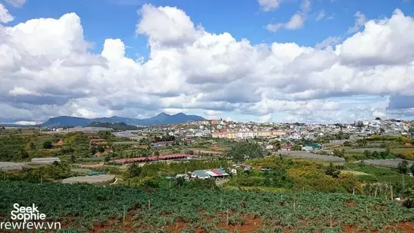 Da Lat hillside panorama with patchwork fields and a mountain town under dramatic clouds, on a 2D1N easy rider route
