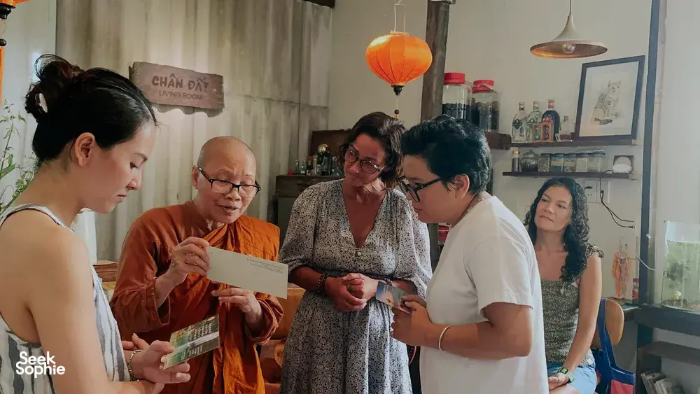 Tamu bersama tuan rumah dan seorang biksu membaca kartu bagan kelahiran Vietnam di Chan Dat Living Room, Hoi An