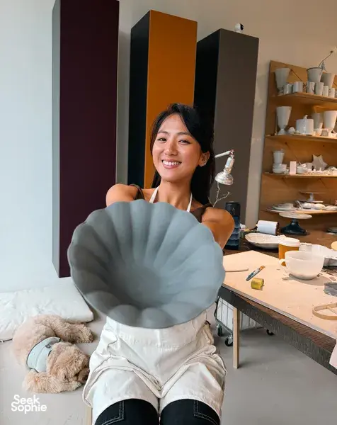 Ina Atelier potter smiling while holding a European-style ceramic plate with scalloped texture in the Singapore studio