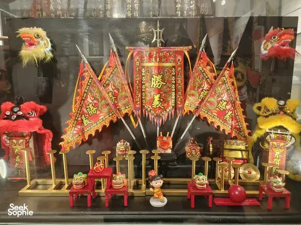Lion dance heritage shop window display with colourful ceremonial banners, lion head figurines and props arranged behind glass