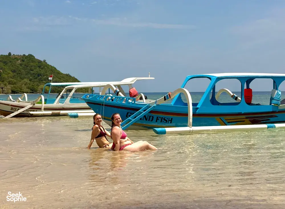 Dua penyelam snorkel meredah air di persisiran menuju bot biru putih, bersedia menerokai perairan Secret Gilis di luar pantai Lombok