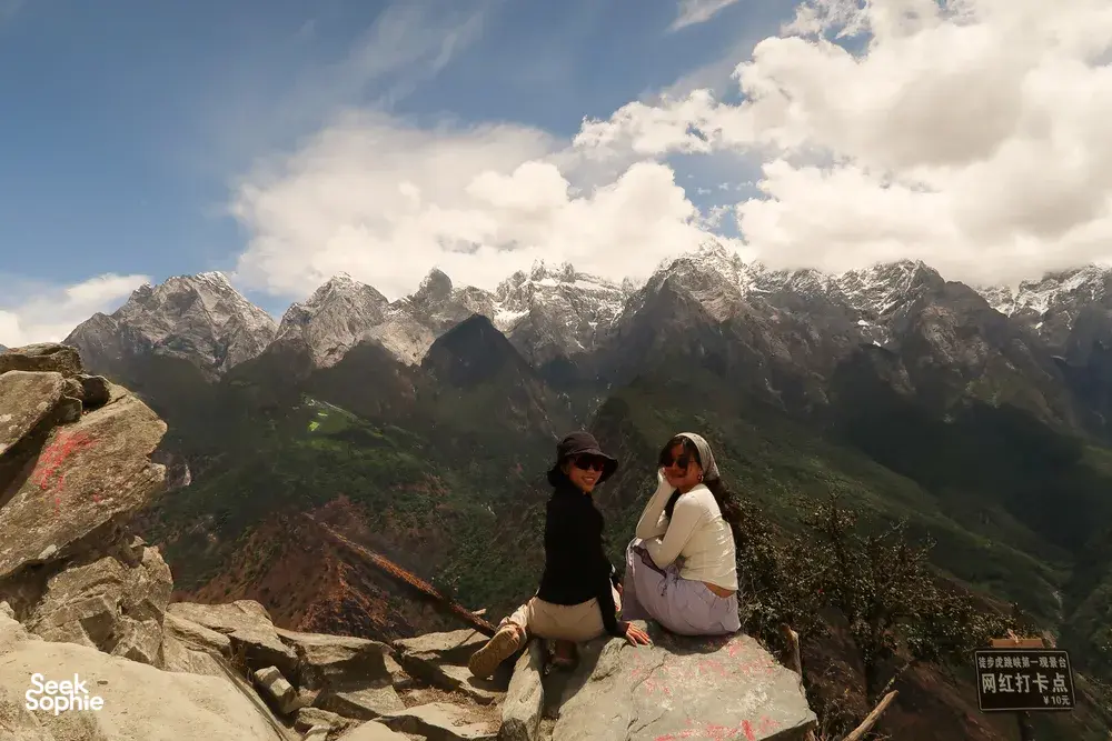 Hikers resting on a cliff overlooking snowcapped peaks above Tiger Leaping Gorge, Lijiang, on a 2D1N high-trail trek