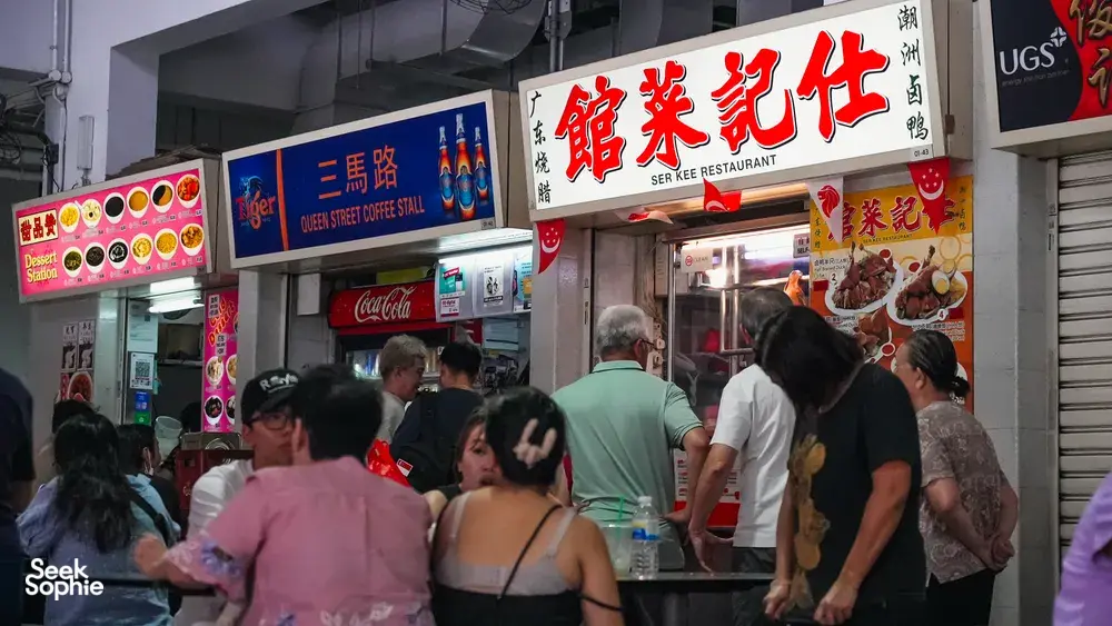 Busier Singapore hawker centre lane with diners queuing in front of street-food stalls under colourful signage — Singapore hidden gems