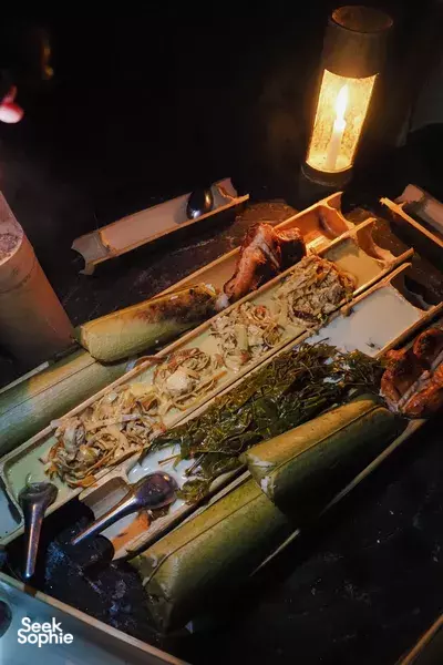 Lantern-lit grill with grilled fish, vegetables and herbs on platters during a Wildest Jungle Cooking Adventure in Khao Sok National Park