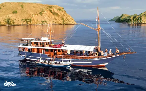 Wooden Fanie Boat Tours liveaboard sailing across calm blue water with passengers on deck on a 3D2N Komodo dive trip Labuan Bajo