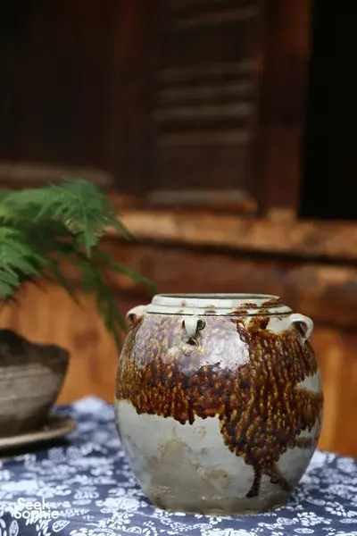 Glazed ceramic storage jar on a patterned cloth inside a traditional wooden room at an ancient pottery village visit in Shangri-La