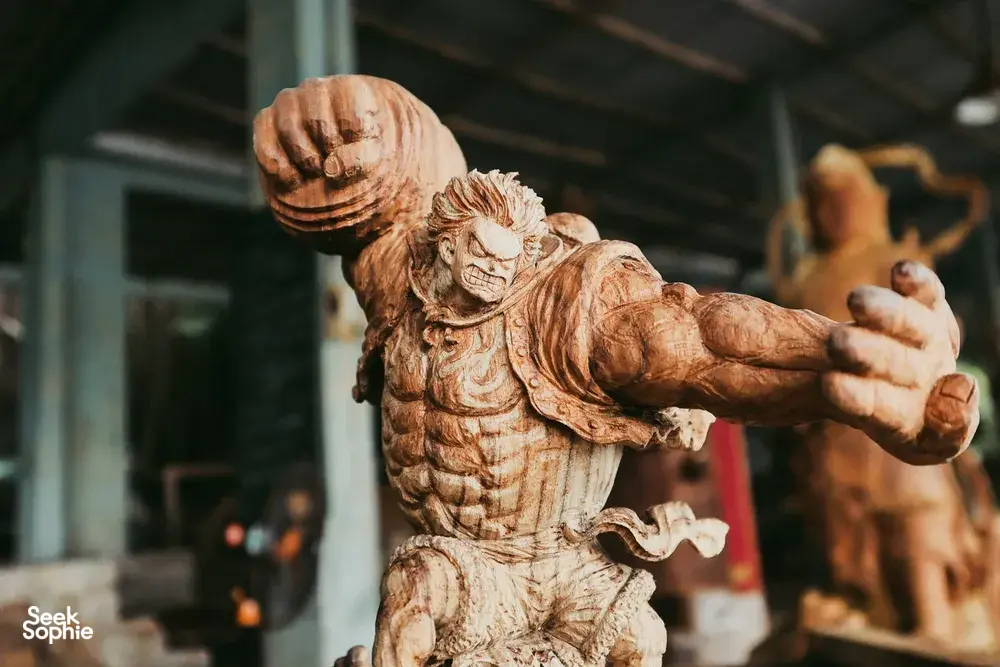 一尊雕刻木制守护像抬起手臂,陈列于会安木雕工坊内