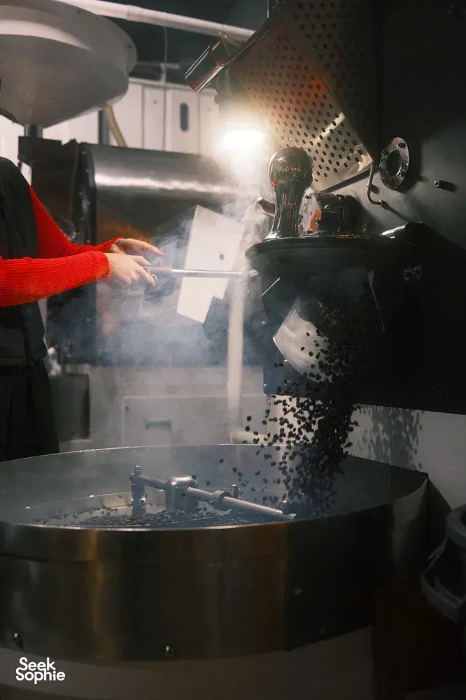Workers operating a hot metal pressing machine in Hoi An, with smoke and paper slips falling as steam fills the chamber