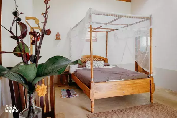 Wooden four-poster bed with white mosquito netting in a Sri Lanka guest room, with potted plants and calm neutral décor