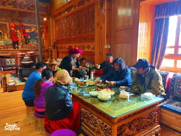 Tibetan home lunch in a warmly decorated room in Shangri-La, with travellers seated around dishes in a host-led meal