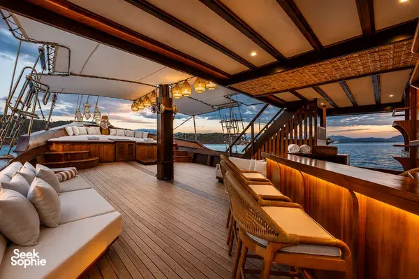 Sunset lounge deck of a Travass Life phinisi with cushioned benches, wooden railings and open sea views, on Komodo Island