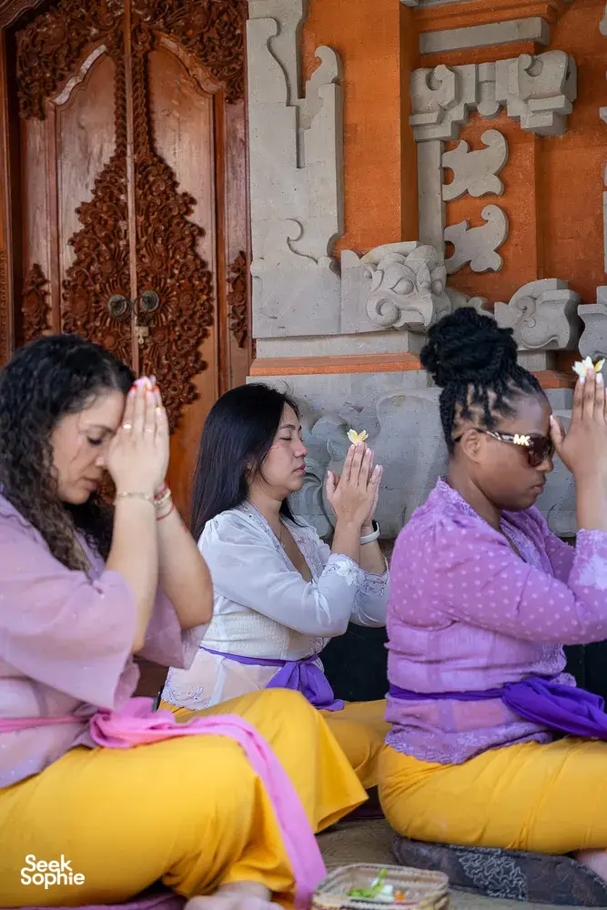 Attendees seated in a Balinese temple praying with hands raised together during canang sari ceremony, Ubud