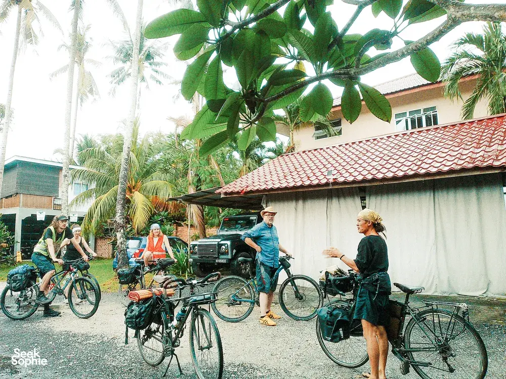 Bicycle Day Langkawi cyclists gather outside a tropical home on Langkawi, with bicycles parked by a red-tiled roof