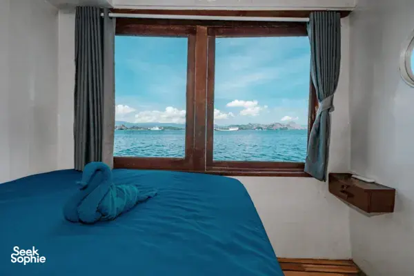 Private 3D2N Komodo cruise cabin with a neatly turned bed by the window, sea and hills visible outside, Labuan Bajo