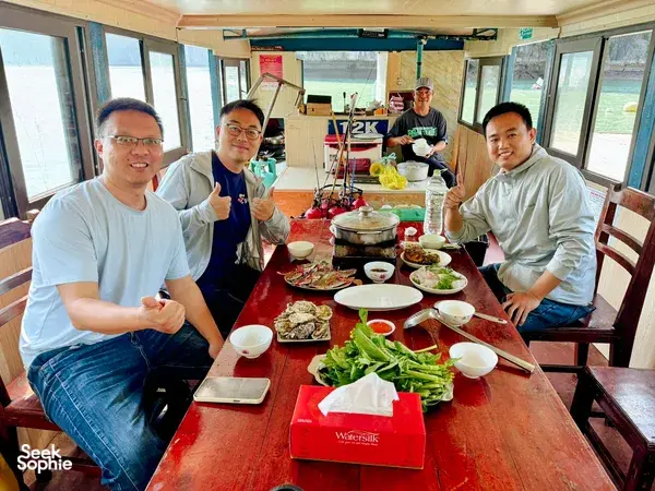 Fish & cook hotpot meal on a boat in Cat Ba, with a group gathered around a steaming red pot and side dishes