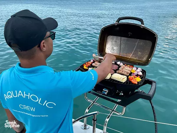 Aquaholic crew member stoking the BBQ on a luxury catamaran deck in Singapore, with open grill facing the sea