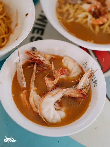 Bowls of prawn noodle soup in orange broth with fresh shrimp, served at an eatery on a Joo Chiat food tour