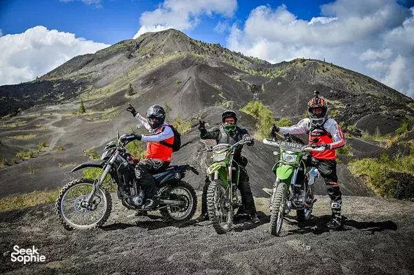 Three enduro riders standing with their bikes on a rocky volcanic slope, mountains behind them, on an adventure to Mt Batur