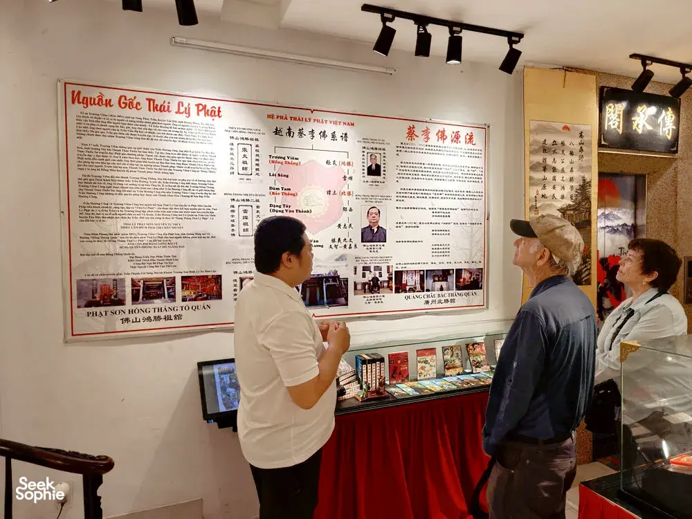 People browse boards and books at a martial arts exhibition, with Vietnamese and Chinese text posters on the walls in Ho Chi Minh City