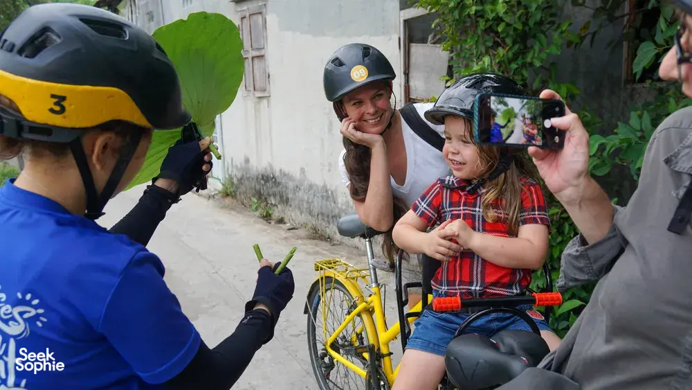 Bike guide taking a selfie with a mother and child beside yellow bicycles on a Mekong Island street near Ho Chi Minh City