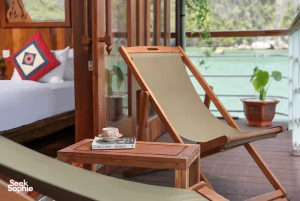 Deck lounge set with a wooden sunbed and small table beside the cabin window, on a boutique cruise in Cat Ba