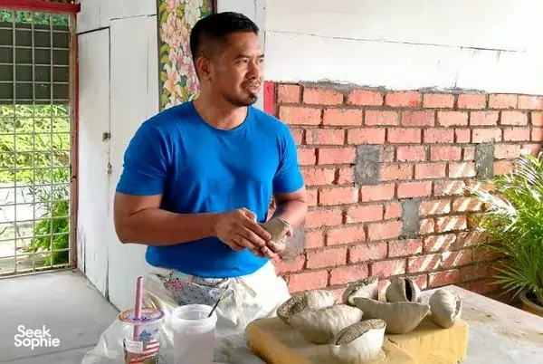 Ceramic artist at Ilham Ceramic Studio in Langkawi teaching pottery, standing by a table of handmade bowls and cups.