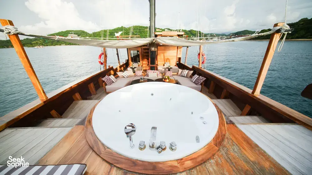 Circular jacuzzi on the wooden deck of a phinisi sailing past the coastline on a Komodo luxe cruise in Labuan Bajo