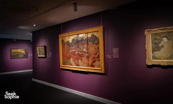 Gallery view with Vietnamese paintings under track lights on purple walls at Quang San Art Museum in Ho Chi Minh City