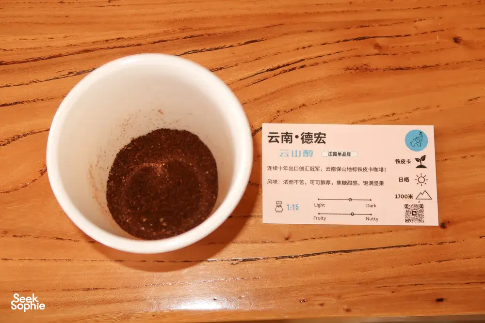 Close-up of a cup of dark coffee grounds beside a Yunnan tasting label card at Seeker Yunnan Coffee Estate in Lijiang