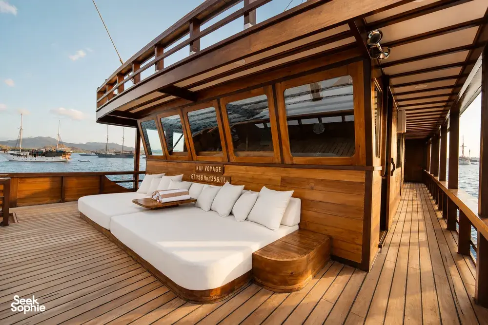 Forward deck sunbed of a Travass Life phinisi with built-in cushions and wooden railings, departing at sunrise in Labuan Bajo