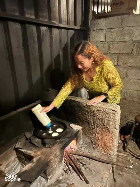 Participant preparing small offerings on a traditional stove inside Rumah Konservasi Kunang Kunang in Bali