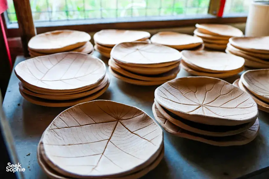 Stacked ceramic plates with etched leaf patterns on a wooden worktable at Ilham Ceramic pottery studio in Langkawi.