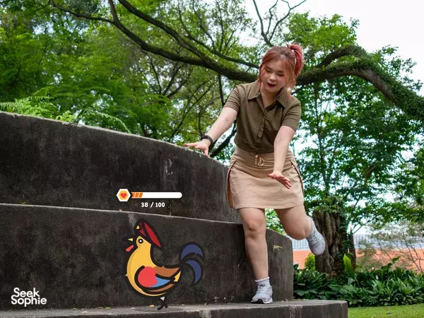 Woman jumping a low wall in Fort Canning during a Puzzle Hunt, with rooster artwork and a progress marker, Singapore