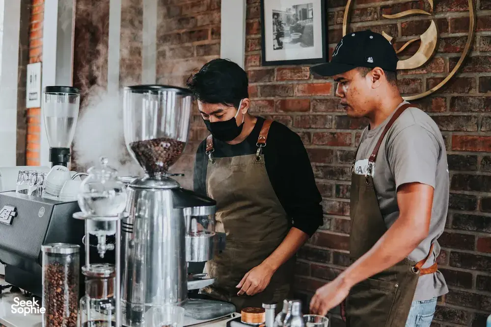 Bali Beans staff preparing coffee with espresso machine steam and grinders on a counter during a workshop in Bali.